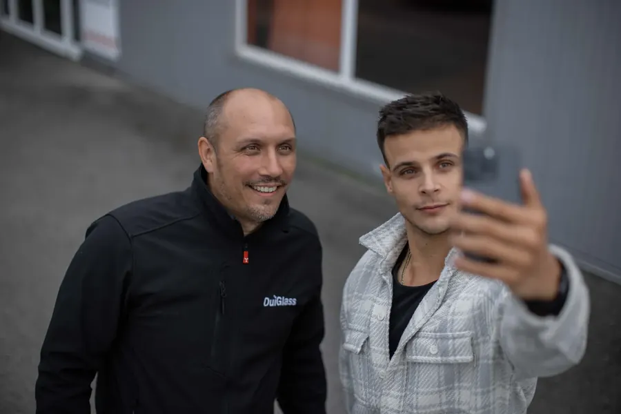 Téléphone à bout de bras, un membre de l'équipe Influmedia fait une prise de vue avec un collaborateur OuiGlass devant un atelier