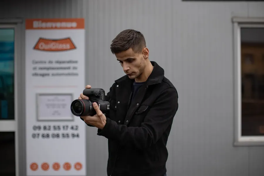 Vidéaste d'Influmedia, appareil en main, devant la devanture d'un centre OuiGlass pendant un tournage en clientèle